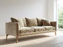 A modern 3-seater sofa in a minimalist living room. The sofa has clean lines, plush cushions, and a soft velvet texture. It sits on wooden legs and is placed against a plain white wall with light wooden (1).webp